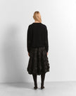 A woman is shown from behind wearing a black long-sleeve knit top and a black textured, ruffled midi skirt with black tights and dark pointed-toe heels, set against a plain white studio background.

Beatrice B- crew neck sweater with embroidered appliques. Available at Edit by Elaine Turner in Houston, TX. Model full back view. 