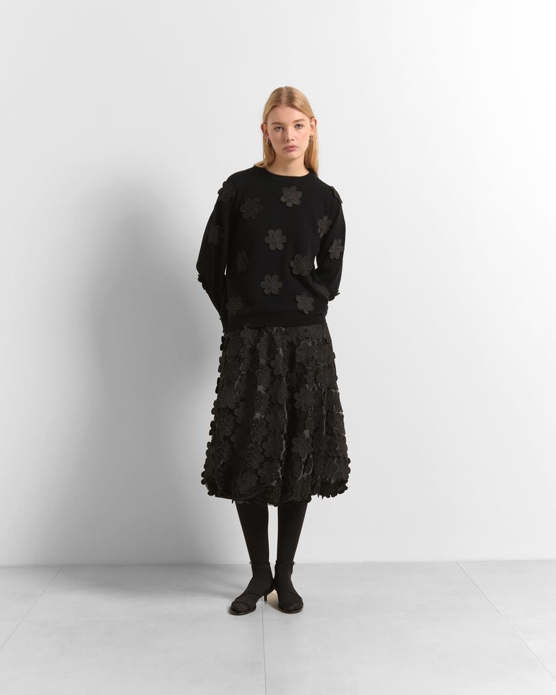 A model stands against a light gray studio background wearing a black long-sleeve knit sweater with tonal floral embroidery and a matching black textured midi skirt.

Beatrice B- crew neck sweater with embroidered appliques. Available at Edit by Elaine Turner in Houston, TX. Model full front view. 