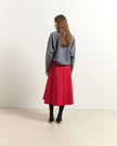 A woman stands with her back to the camera wearing a gray knit sweater and a bright red midi skirt, paired with black tights and black ankle boots, in a minimalist studio setting.

Beatrice B Flared Midi Skirt Red. Available at Edit by Elaine Turner in Houston, TX. Full back model view. 