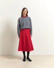 A model stands in a studio wearing a gray knit sweater with a red and navy striped mock neck collar, paired with a bright red A-line midi skirt, black tights, and black heeled boots.

Beatrice B Flared Midi Skirt Red. Available at Edit by Elaine Turner in Houston, TX. Full front model view. 