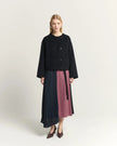 A model stands against a light beige studio background wearing a black cropped cardigan and a pleated midi skirt with color-blocked panels in dark navy and dusty rose. She is wearing dark brown pointed-toe heels.

Beatrice B Pleated Midi Skirt with Panels in Raspberry Pink. Available at Edit by Elaine Turner in Houston, TX. Full front Model View. 