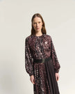 A woman modeling a long-sleeved midi dress with a burnt amber abstract spotted pattern, featuring a black belt at the waist, set against a plain light gray studio background.

Beatrice B Printed Silk Midi Dress with Pleats. Available at Edit by Elaine Turner in Houston, TX. Close up model view. 