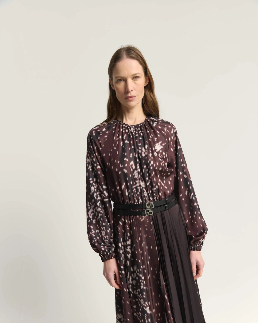 A woman modeling a long-sleeved midi dress with a burnt amber abstract spotted pattern, featuring a black belt at the waist, set against a plain light gray studio background.

Beatrice B Printed Silk Midi Dress with Pleats. Available at Edit by Elaine Turner in Houston, TX. Close up model view. 