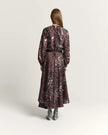 A woman viewed from the back wearing a long-sleeve midi dress with a burnt amber abstract floral pattern, a black waist belt, and gray pointed-toe heels, set against a plain light gray studio background.

Beatrice B Printed Silk Midi Dress with Pleats. Available at Edit by Elaine Turner in Houston, TX. Full back model view. 