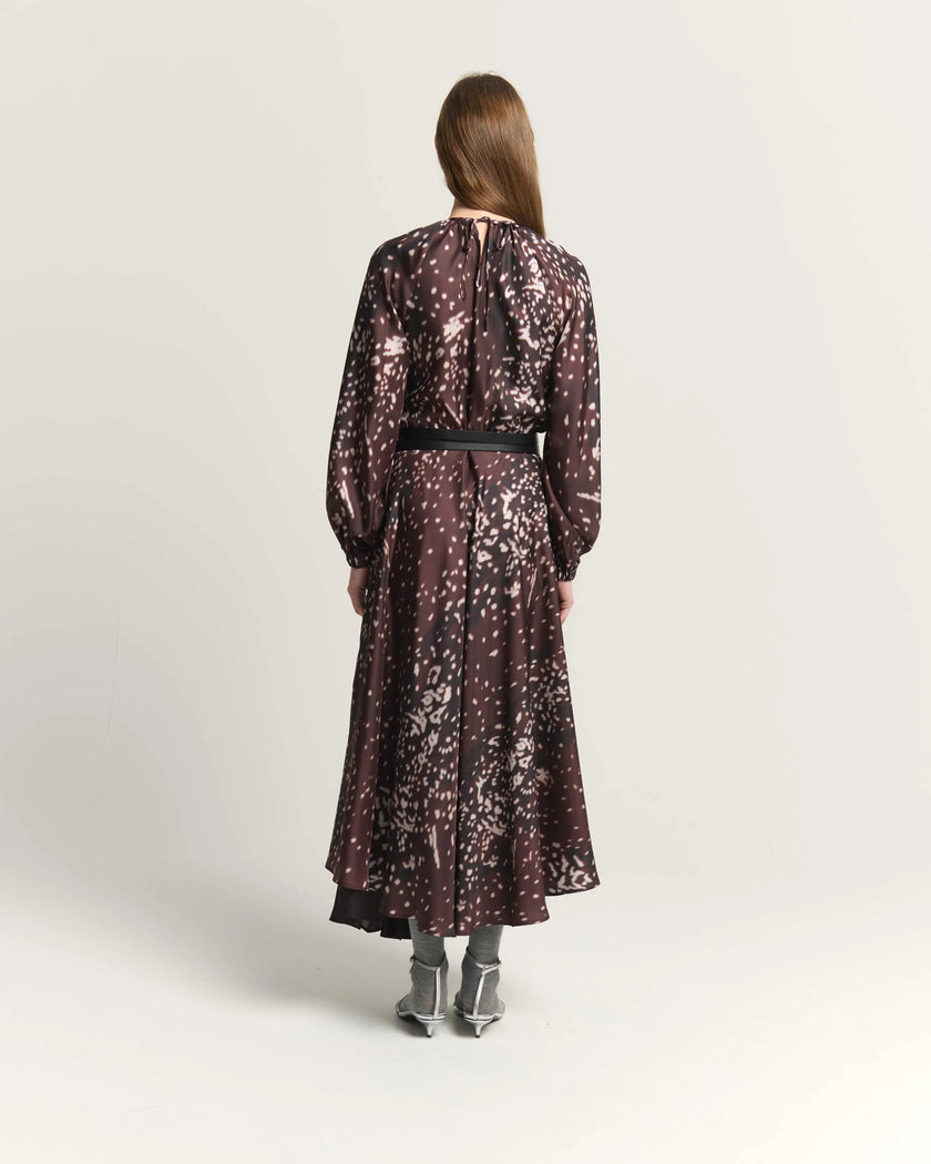 A woman viewed from the back wearing a long-sleeve midi dress with a burnt amber abstract floral pattern, a black waist belt, and gray pointed-toe heels, set against a plain light gray studio background.

Beatrice B Printed Silk Midi Dress with Pleats. Available at Edit by Elaine Turner in Houston, TX. Full back model view. 