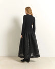 A woman stands with her back to the camera wearing a long-sleeved black ribbed top and a full black skirt with a subtle tonal pattern, set against a plain off-white studio background.

Beatrice B. Ribbed Knit Dress with Jacquard Skirt in black. Available at Edit by Elaine Turner in Houston, TX. Full Model Back View.