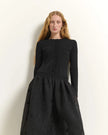 A model with long light-brown hair wearing a black ribbed long-sleeve top with front buttons and a matching textured black skirt, standing against a plain off-white wall.

Beatrice B. Ribbed Knit Dress with Jacquard Skirt in black. Available at Edit by Elaine Turner in Houston, TX. Model close up View.