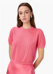 Woman wearing a pink knitted top against a white background by CAMI NYC - Ellory Cotton Knit Top in Hibiscus at edit. BY ELAINE TURNER. Model shown wearing the Ellory from the front view. 