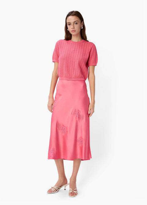 Woman wearing a pink knitted top against a white background by CAMI NYC - Ellory Cotton Knit Top in Hibiscus at edit. BY ELAINE TURNER. Model shown wearing the Ellory with a full body front view. 