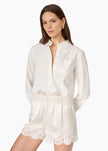 A woman modeling a white long-sleeve collared shirt with matching white shorts featuring delicate lace trim at the waist and hem, set against a plain white studio background.

CAMI NYC Napier Shirt in white. Available at Edit by Elaine Turner in Houston, TX. Full front model close up view. 
