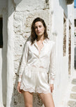 A woman stands outdoors against a sunlit white stucco wall wearing a white cotton poplin long-sleeve shirt and matching shorts with lace trim.

CAMI NYC Napier Shirt in white. Available at Edit by Elaine Turner in Houston, TX. Full front model view. 