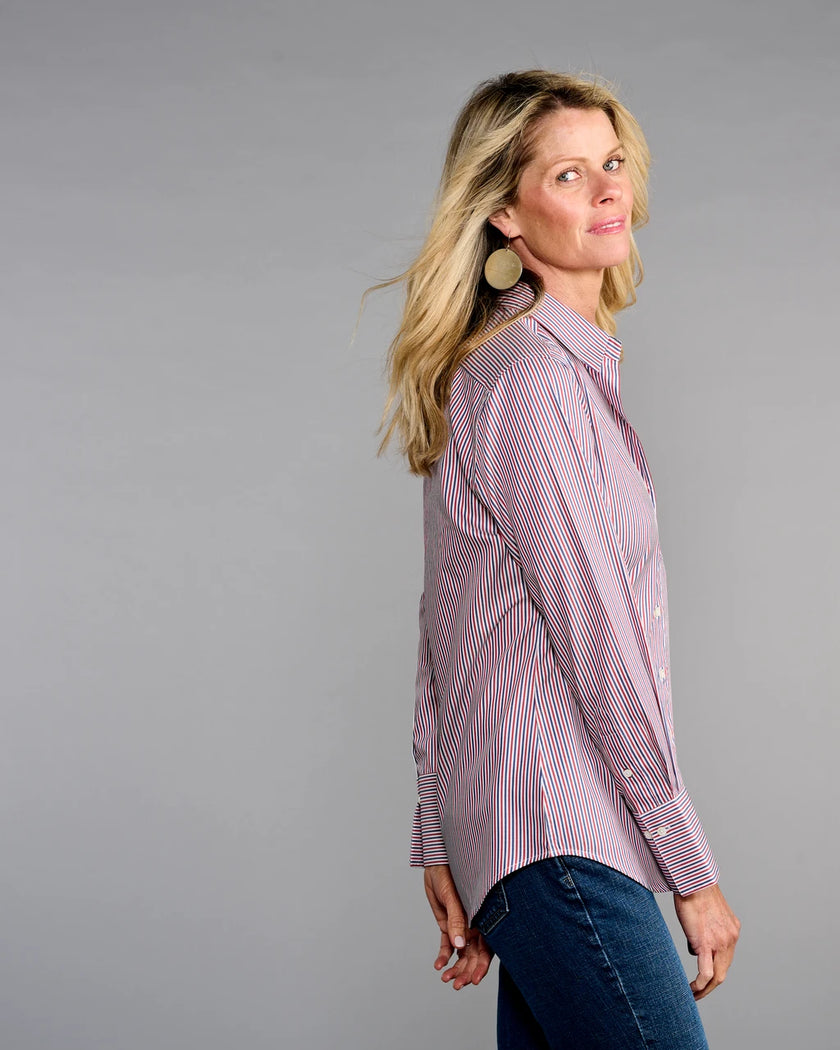 A woman modeling a long-sleeve button-up shirt with thin red and blue vertical stripes on a light pinkish-purple base, paired with dark blue jeans, against a solid gray studio background.

Claridge & King- The 4..0 Shirt in Ross Stripe. Available at Edit by Elaine Turner in Houston, TX. Model Side View 