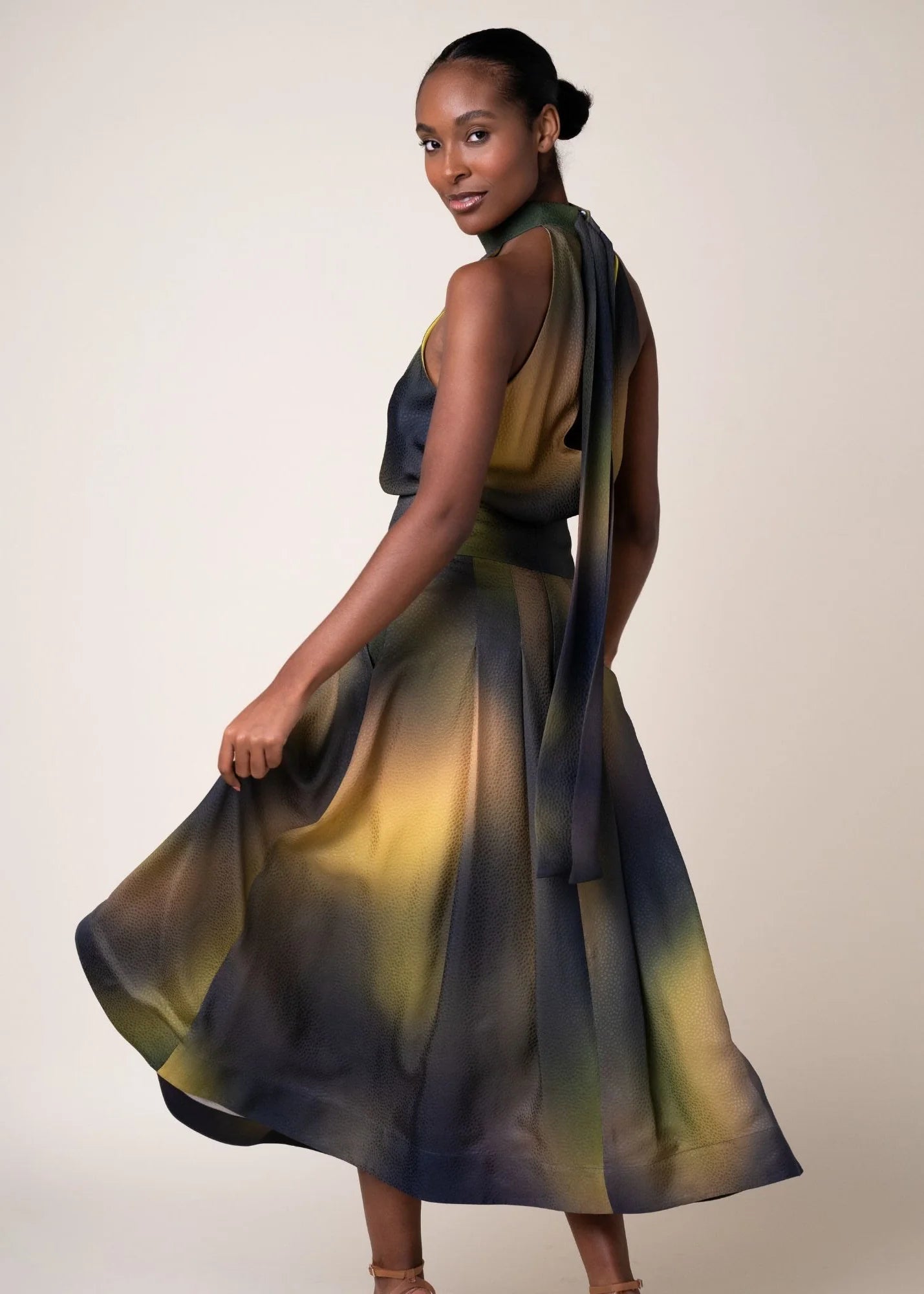 A woman modeling a sleeveless Sabrina halter blouse with a flowing skirt, featuring a dark slate blue and olive green watercolor-like gradient on a light beige studio background.

Daniel Gonzalez Chiqui Drop-Waist Pleated Skirt Octopus Print. Available at Edit by Elaine Turner in Houston, TX. Back Model View. 