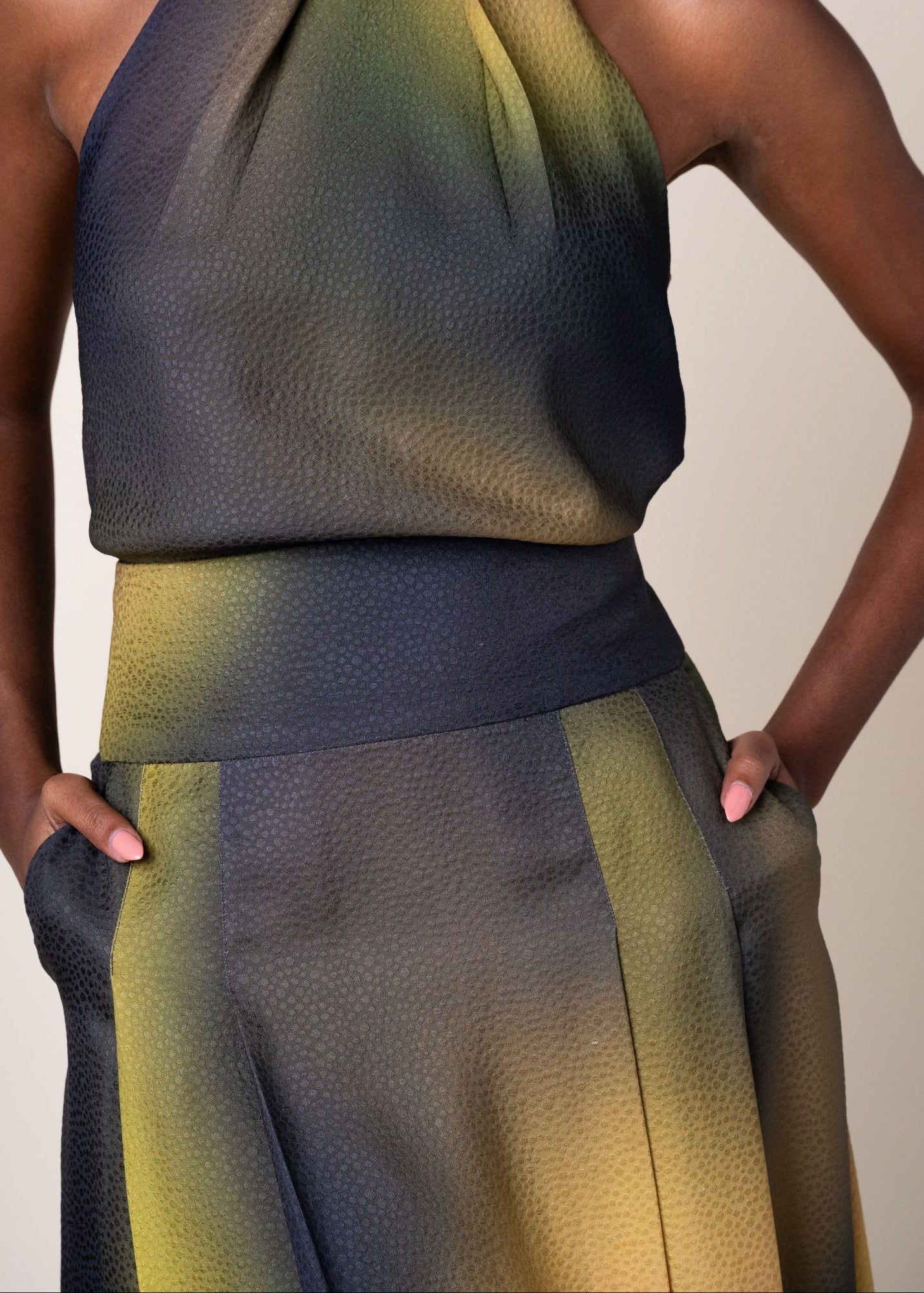 Close-up of a model wearing a textured halter top and matching wide-leg skirt in a dark slate blue-gray with olive green and mustard yellow gradient 
panels.

Daniel Gonzalez Chiqui Drop-Waist Pleated Skirt Octopus Print. Available at Edit by Elaine Turner in Houston, TX. Front Close Up Model View. 