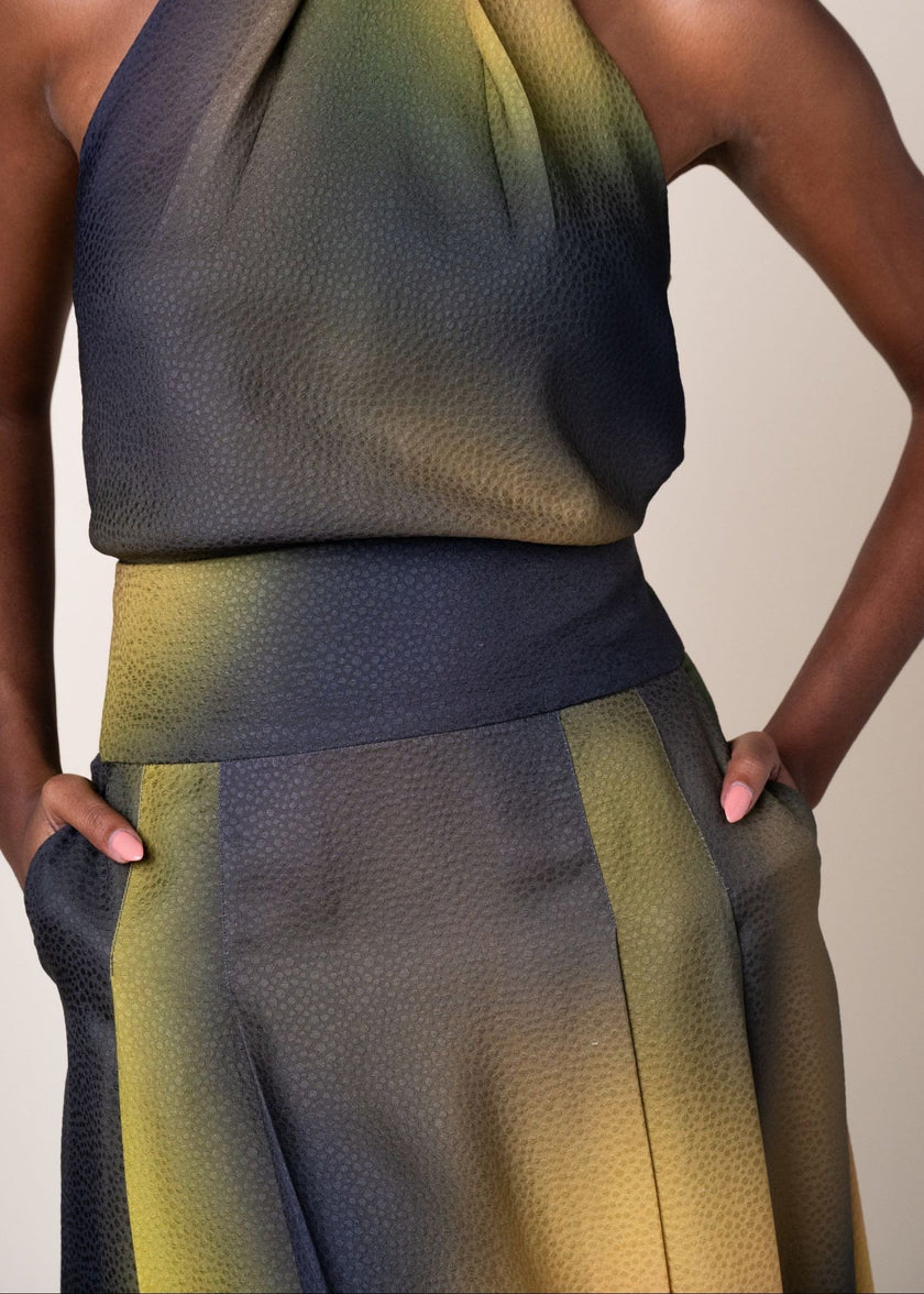 Close-up of a model wearing a textured halter top and matching wide-leg skirt in a dark slate blue-gray with olive green and mustard yellow gradient 
panels.

Daniel Gonzalez Chiqui Drop-Waist Pleated Skirt Octopus Print. Available at Edit by Elaine Turner in Houston, TX. Front Close Up Model View. 
