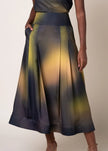 A woman wearing a high-waisted midi skirt with a gradient pattern of dark navy, yellow, and olive green, paired with a matching top against a plain beige background.

Daniel Gonzalez Chiqui Drop-Waist Pleated Skirt Octopus Print. Available at Edit by Elaine Turner in Houston, TX. Front Model View. 