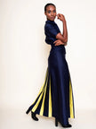 A model wearing a navy blue silk-cotton blend maxi dress with yellow and navy vertical pleated stripes on the skirt, paired with black heels, against a plain off-white studio background.

Daniel Gonzalez Ella Asymmetrical Pleated Dress in Deep Ocean. Available at Edit by Elaine Turner in Houston, TX. Full model front size view. 