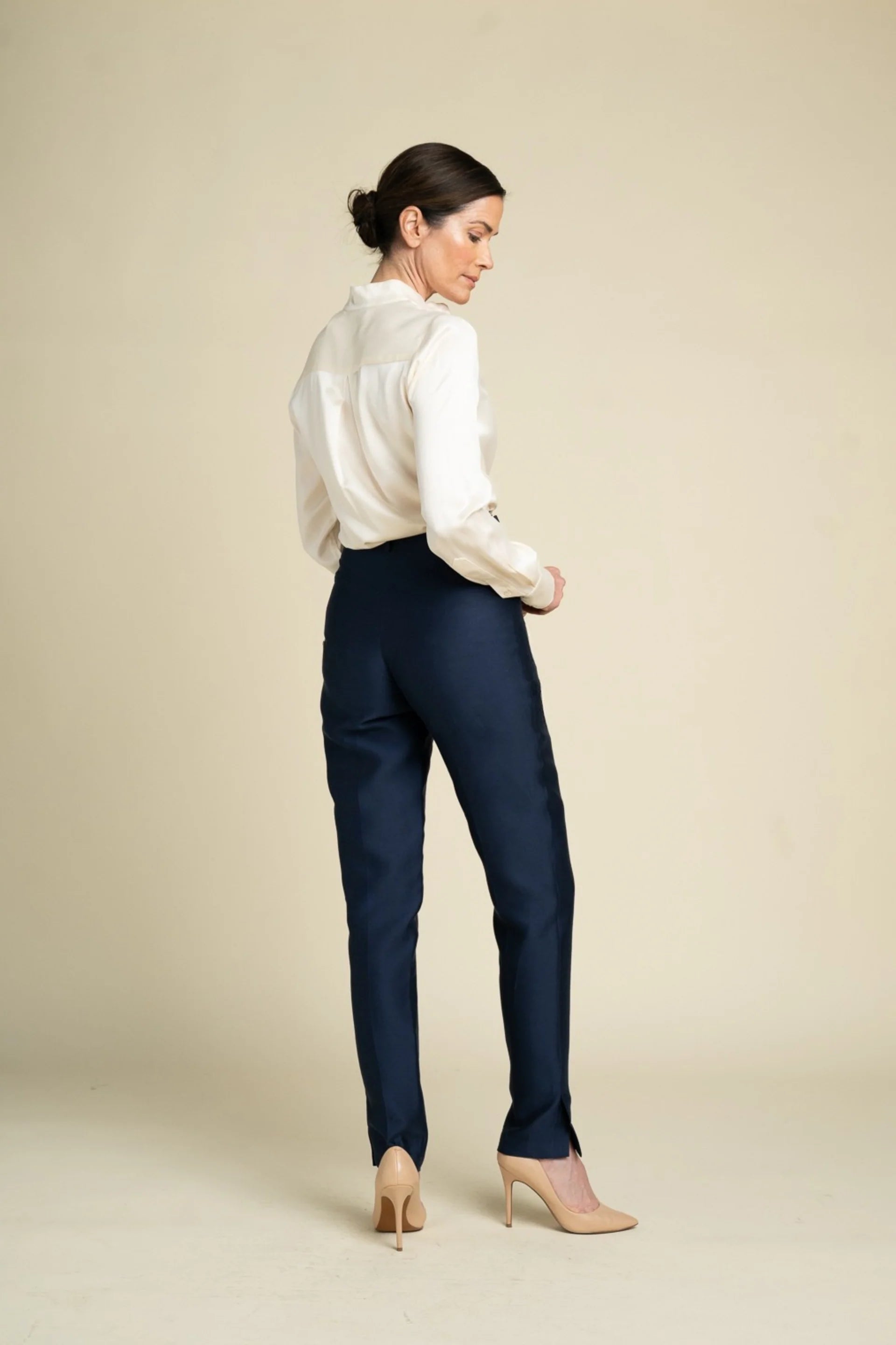 A woman shown from the back wearing navy blue trousers, a white blouse, and beige heels against a plain beige studio background.

Daniel Gonzalez Marina Blouse in Foam. Available at Edit by Elaine Turner in Houston, TX. Back Model View. 