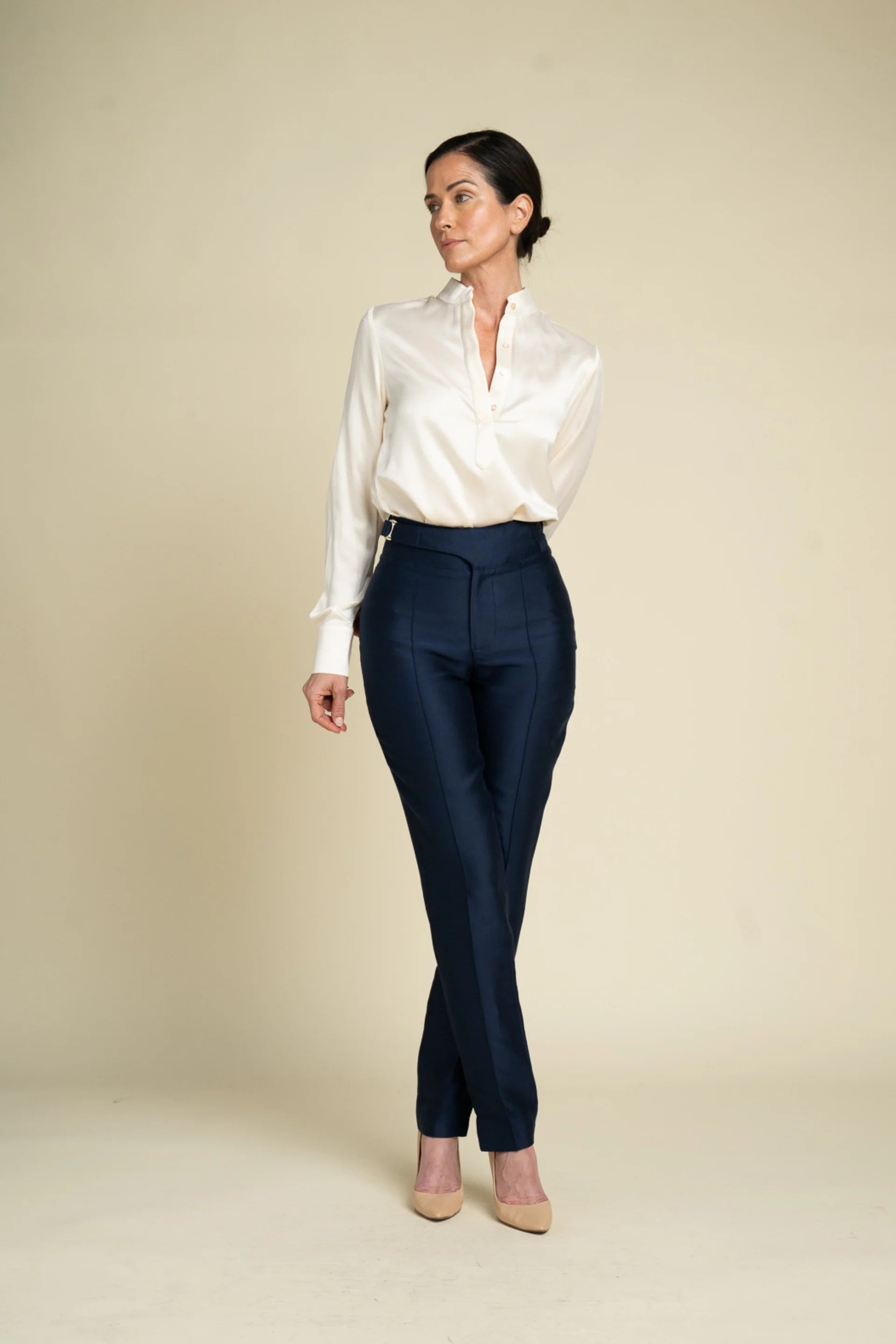 A woman modeling a white satin button-down shirt tucked into high-waisted navy trousers, standing against a solid beige studio background.

Daniel Gonzalez Marina Blouse in Foam. Available at Edit by Elaine Turner in Houston, TX. Front Model View. 