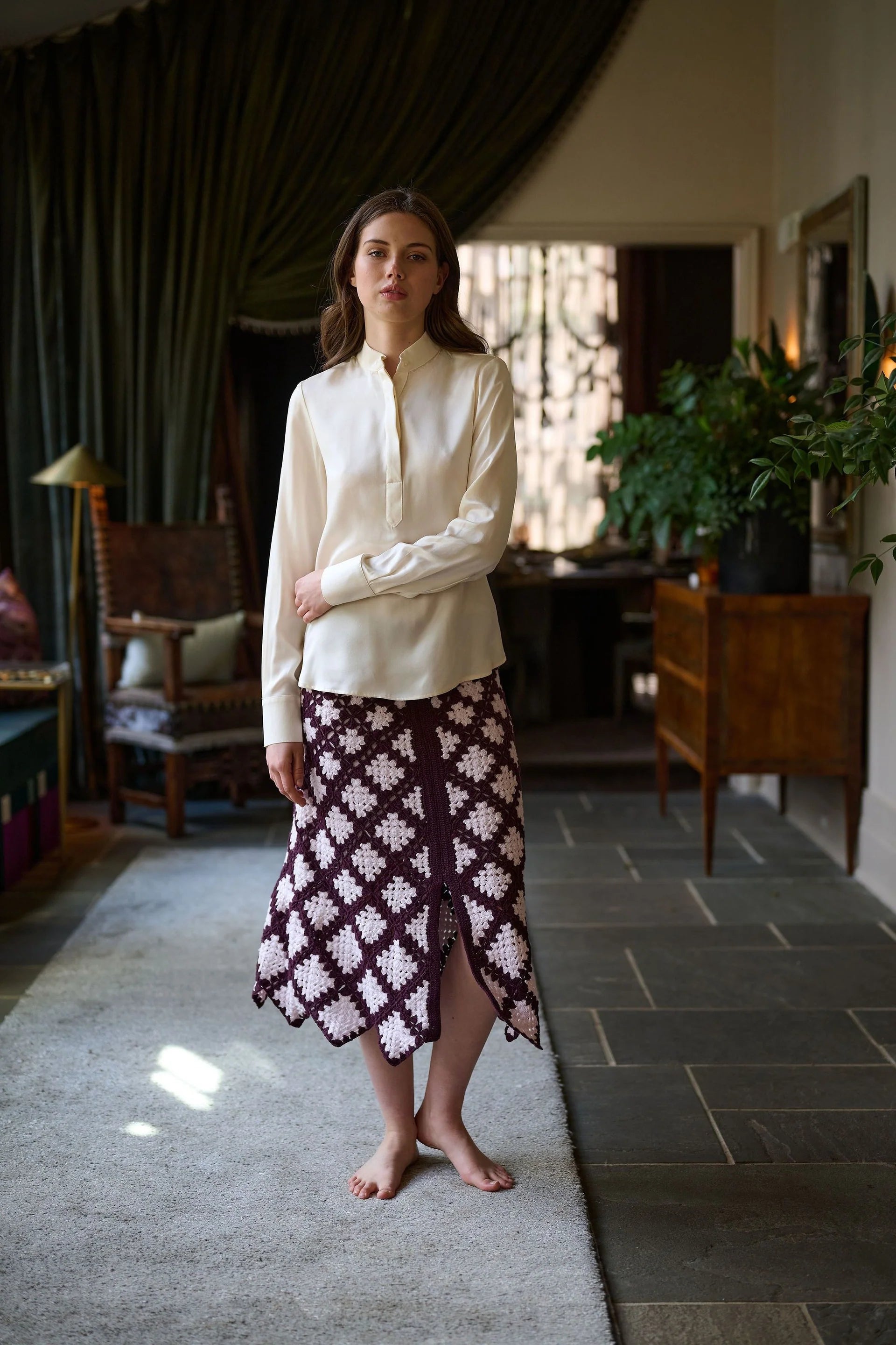 Woman in a white blouse and patterned skirt standing in a room with dark curtains and wooden furniture.

Daniel Gonzalez Marina Blouse in Foam. Available at Edit by Elaine Turner in Houston, TX. Full front model view. 