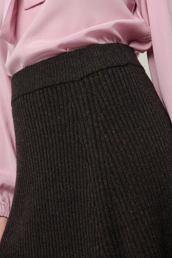 Close-up of a dark charcoal ribbed knit skirt paired with a light pink satin 
blouse.

Dea Kudibal- Alesandra knit skirt dusty chocolate. Available at Edit by Elaine Turner in Houston, TX. Close Up View. 