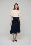 A woman modeling a cream short-sleeve top and a dark navy midi skirt with button details on the side, standing against a light gray studio background.

Dea Kudibal - Giselle Denim Skirt - Dark Blue. Available at Edit by Elaine Turner in Houston, TX.  Model Full Front View. 