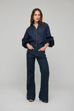 A woman modeling a dark navy blue two-piece set consisting of a long-sleeve button-up blouse with puffed shoulders and matching high-waisted, wide-leg trousers featuring a small geometric pattern, shot against a solid light gray background.

Dea Kudibal Monia Blouse Chambray Blue. Available at Edit by Elaine Turner in Houston, TX . Full Model Front View. 