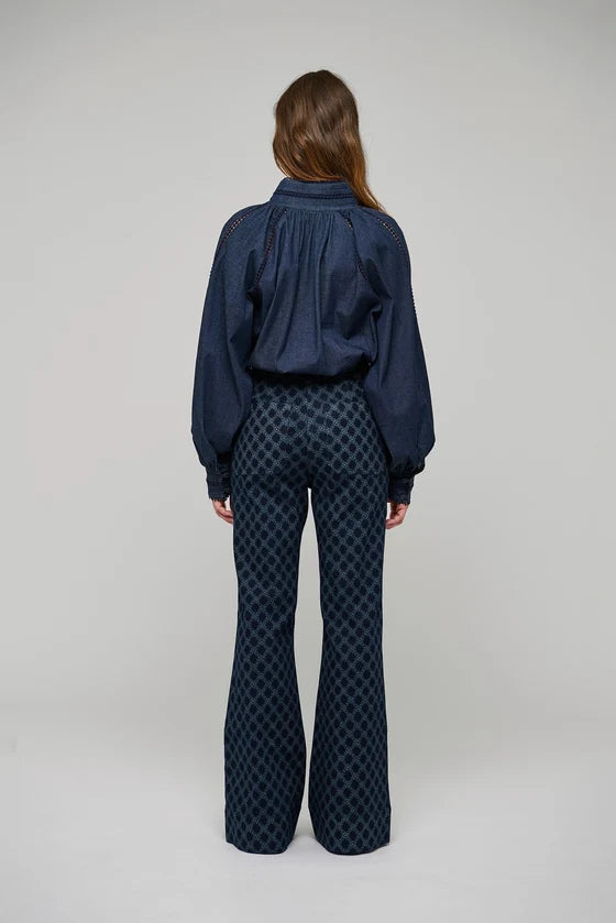 A model viewed from the back wearing a dark navy blue long-sleeve blouse with a gathered back and dark navy patterned flared pants, set against a plain light gray studio background.

Dea Kudibal Monia Blouse Chambray Blue. Available at Edit by Elaine Turner in Houston, TX . Model Back View. 