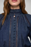 Close-up of a model wearing a dark blue denim blouse with a high gathered neckline, front button placket, and decorative geometric embroidered trim.

Dea Kudibal Monia Blouse Chambray Blue. Available at Edit by Elaine Turner in Houston, TX . Model Close Up View. 