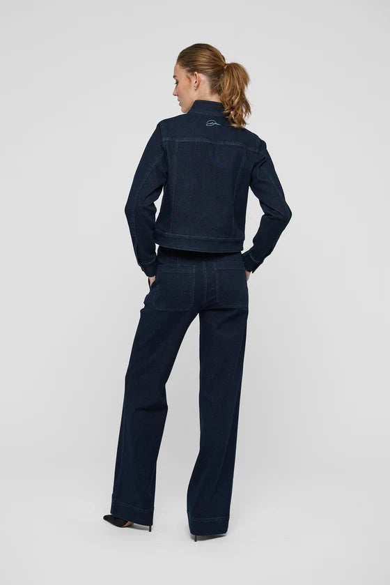 A woman stands with her back to the camera wearing a dark navy blue denim jacket and matching wide-leg denim pants against a light gray studio 
background.

Dea Kudibal- Wilma Denim Jacket Dark Blue. Available at Edit by Elaine Turner in Houston, TX. Full model back view. 