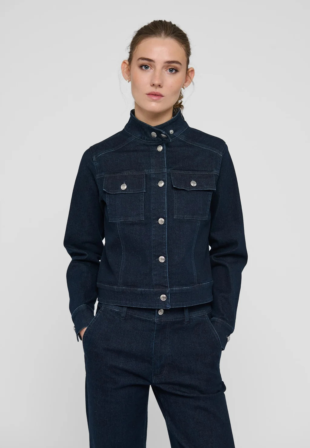A woman modeling a dark navy blue denim jacket and matching dark denim pants against a light gray studio background.

Dea Kudibal- Wilma Denim Jacket Dark Blue. Available at Edit by Elaine Turner in Houston, TX. Model full front view. 