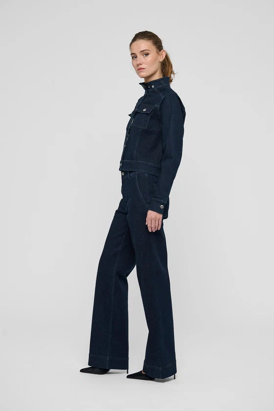 A model wearing a dark navy blue denim jacket and matching wide-leg denim pants, shown in profile against a light gray studio background.

Dea Kudibal- Wilma Denim Jacket Dark Blue. Available at Edit by Elaine Turner in Houston, TX. Full Model Side view. 