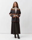 A model stands against a light gray studio background wearing a dark patterned jacket with brown and beige stripes, a cream turtleneck, a long dark skirt, and dark ankle boots.

Diega Virato Jacket in anthracite. Available at Edit by Elaine Turner in Houston, TX. Full front model view. 