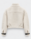 Back view of a cropped, textured bouclé jacket in cream beige, featuring black stripe trim and gold buttons on the sleeve cuffs, set against a light gray background.

Edward Achour - Cropped Contrast Trim Boucle Jacket in beige & black. Available at Edit by Elaine Turner in Houston, TX. Back flat lay view. 