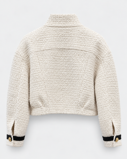 Back view of a cropped, textured bouclé jacket in cream beige, featuring black stripe trim and gold buttons on the sleeve cuffs, set against a light gray background.

Edward Achour - Cropped Contrast Trim Boucle Jacket in beige & black. Available at Edit by Elaine Turner in Houston, TX. Back flat lay view. 