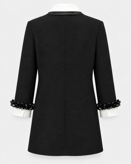 Black blazer with structured shoulders, a notched collar, and decorative black beaded ruffle trim at the cuffs, shown from the back on a white mannequin against a light gray background.

Edward Achour Extended Length Shift Dress with Contrast Bib in Black. Available at Edit by Elaine Turner in Houston, TX. Back flat lay view. 
