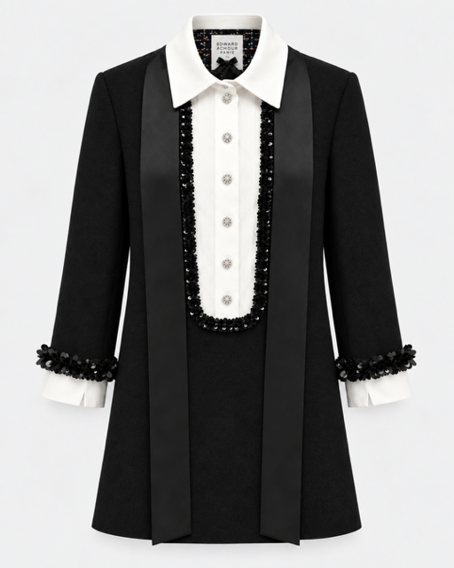 A black structured tuxedo-style dress with a white shirt collar, white front buttons, black beaded trim, and matching black beaded cuffs, shown on a light gray background.

Edward Achour Extended Length Shift Dress with Contrast Bib in Black. Available at Edit by Elaine Turner in Houston, TX. Front flat lay view. 