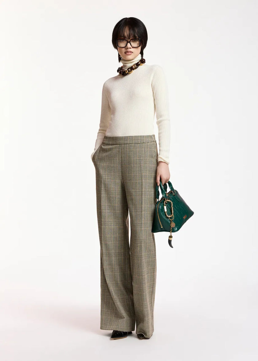 A model stands against a plain white studio background wearing a cream turtleneck sweater, wide-leg olive plaid trousers, a chunky brown necklace, and holding a dark green handbag.

Essentiel Antwerp - Kelmuse Knitted Pullover - Off White. Available at Edit by Elaine Turner in Houston, TX. Full model front view. 