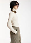 A model in profile wearing a cream ribbed turtleneck sweater, brown plaid trousers, and a chunky brown chain necklace, set against a plain white studio background.

Essentiel Antwerp - Kelmuse Knitted Pullover - Off White. Available at Edit by Elaine Turner in Houston, TX. Model side view. 