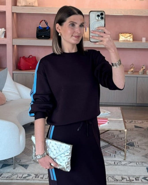 Woman taking a selfie in a stylish outfit in a pink interior setting with shelves and decor at edit. BY ELAINE TURNER wearing PINKO striped arm sweatshirt that goes with the skirt. 