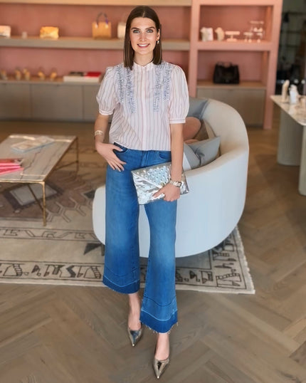 Woman in a stylish outfit , top from Essentiel Antwerp brand, ruffle and rhinestone top and Le Jean denim, plius an Elaine Turner silver studded leather handbag, Bella Clutch. She is standing in a modern interior setting at edit. BY ELAINE TURNER boutique in Houston, Tx. 