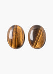 A pair of oval stud earrings made from polished tiger's eye, showing characteristic golden-brown and black banded patterns, set against a plain white background.

Jennifer Behr- Audra Earrings - Tigers Eye. Available at Edit by Elaine Turner in Houston, TX. 