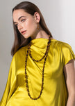 A woman wearing a bright yellow draped top and a long dark brown beaded necklace, photographed against a plain light gray studio background.

Jennifer Behr- Veda Necklace - Tigers Eye. Available at Edit by Elaine Turner in Houston, TX. Model View. 