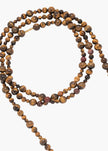 A multi-strand beaded necklace made of polished tiger's eye beads, arranged in a loose circle on a plain light gray background.

Jennifer Behr- Veda Necklace - Tigers Eye. Available at Edit by Elaine Turner in Houston, TX.