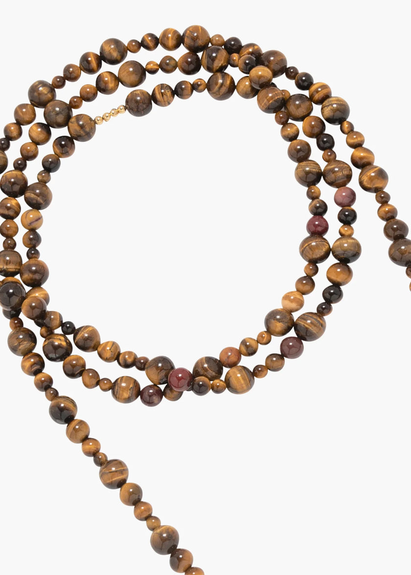 A multi-strand beaded necklace made of polished tiger's eye beads, arranged in a loose circle on a plain light gray background.

Jennifer Behr- Veda Necklace - Tigers Eye. Available at Edit by Elaine Turner in Houston, TX.