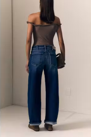 A woman shown from the back wearing a brown off-the-shoulder top, wide-leg blue jeans, and brown shoes, holding a dark brown handbag in a minimalist indoor setting.

Le Jean- Baby Bootcut - Diamond In The Rough. Available at Edit by Elaine Turner in Houston, TX. Back Model View. 