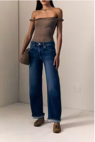 A model wearing a brown off-the-shoulder top, wide-leg blue jeans, and brown suede loafers, holding a small brown handbag against a minimalist beige background.

Le Jean- Baby Bootcut - Diamond In The Rough. Available at Edit by Elaine Turner in Houston, TX. Front Model View. 