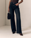 A model wearing dark blue wide-leg denim jeans, holding a small black handbag, standing in a minimalist beige room corner.

Le Jean- Column Jean - Fade to Black 
Model Close Up view. Available at Edit by Elaine Turner in Houston, TX. 