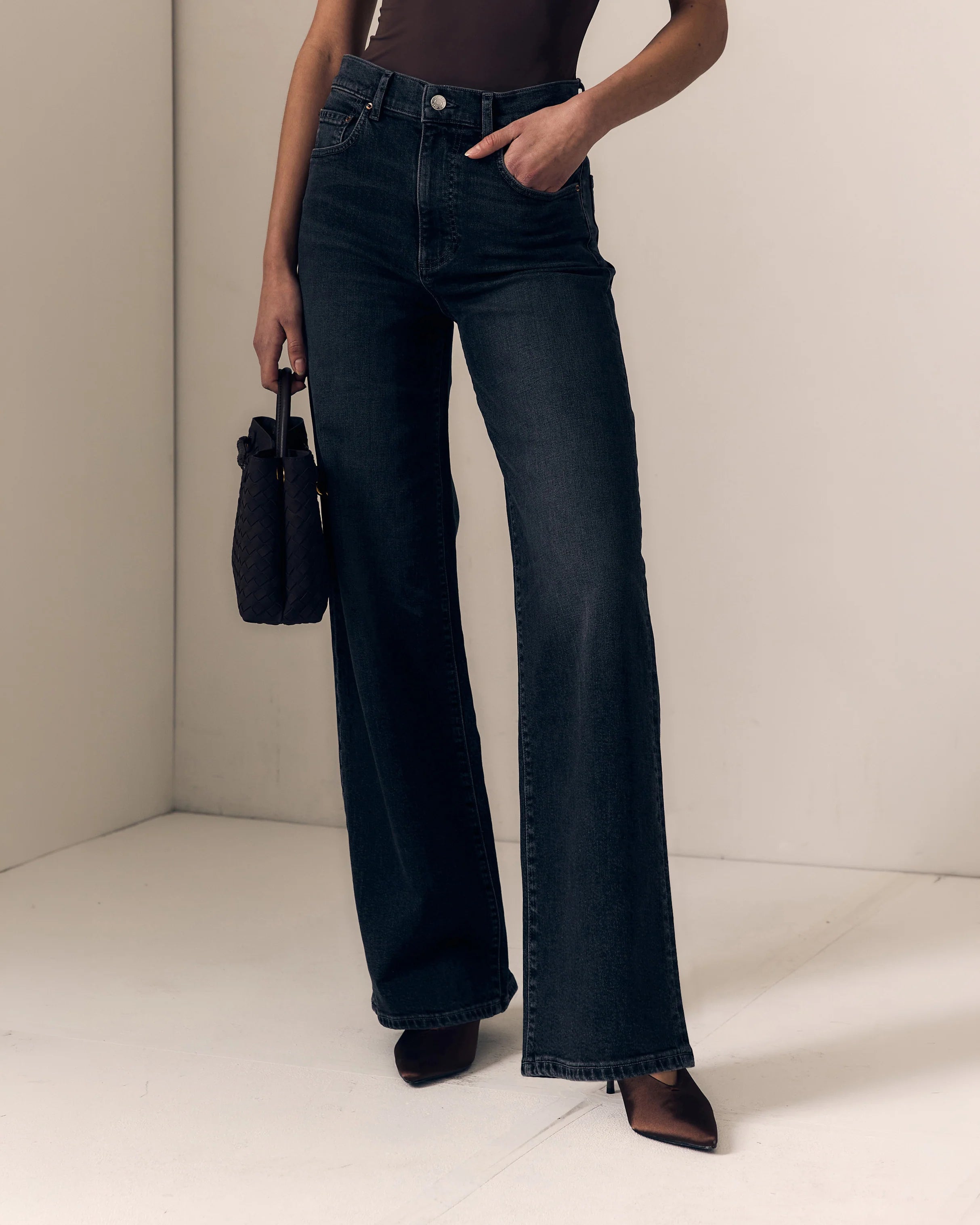 A model wearing dark blue wide-leg denim jeans, holding a small black handbag, standing in a minimalist beige room corner.

Le Jean- Column Jean - Fade to Black 
Model Close Up view. Available at Edit by Elaine Turner in Houston, TX. 