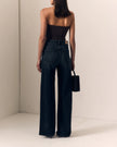 A model shown from behind wearing dark wide-leg denim jeans, a black strapless top, and holding a small black handbag in a minimalist beige room.

Le Jean- Column Jean - Fade to Black 
Full model back view. Available at Edit by Elaine Turner in Houston, TX. 